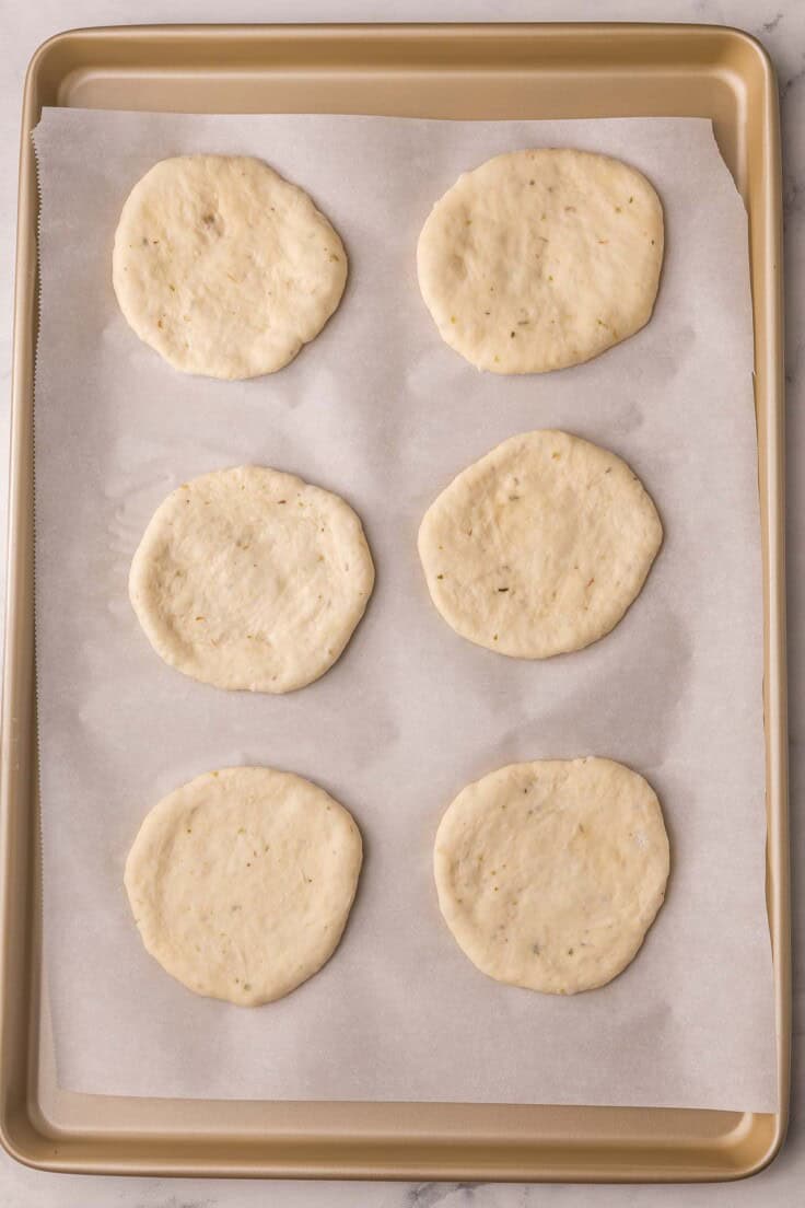 six small unbaked pizza crusts on a parchment lined pan.