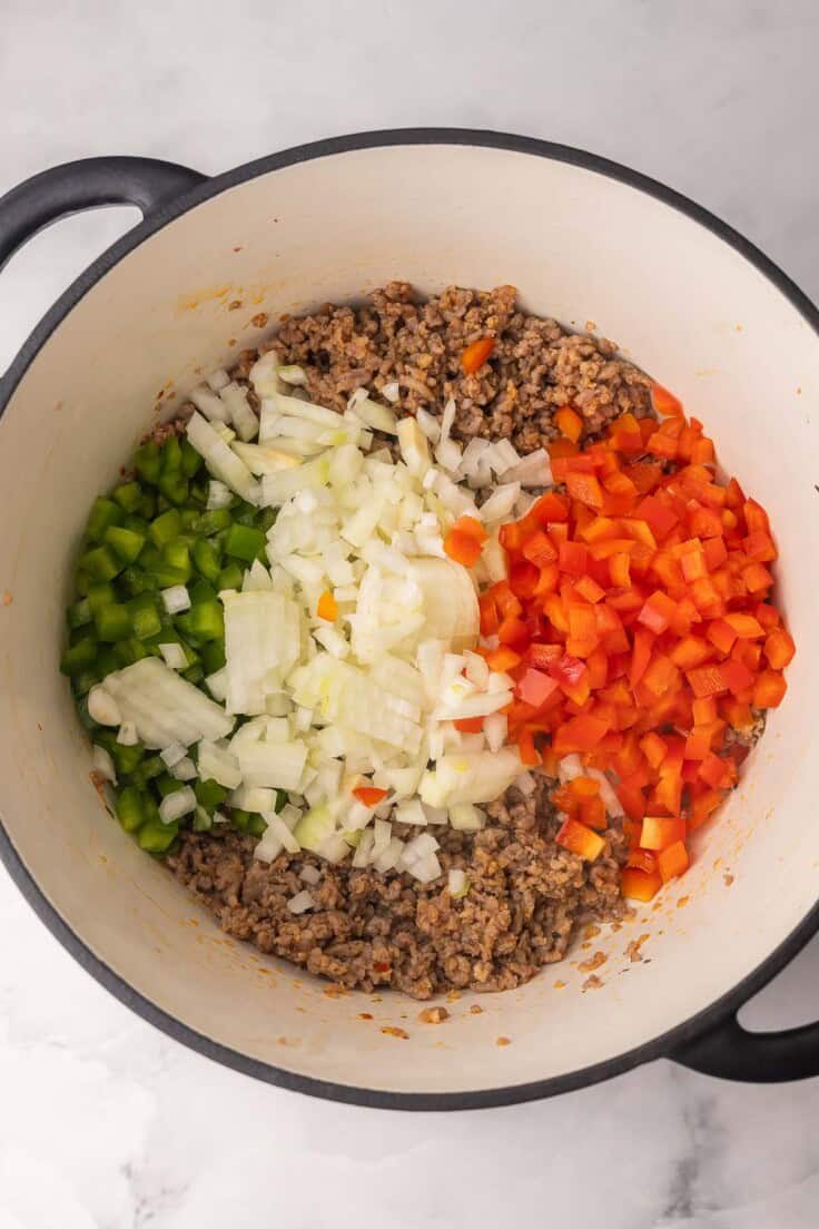chopped vegetables in large pot with cooked italian sausage.