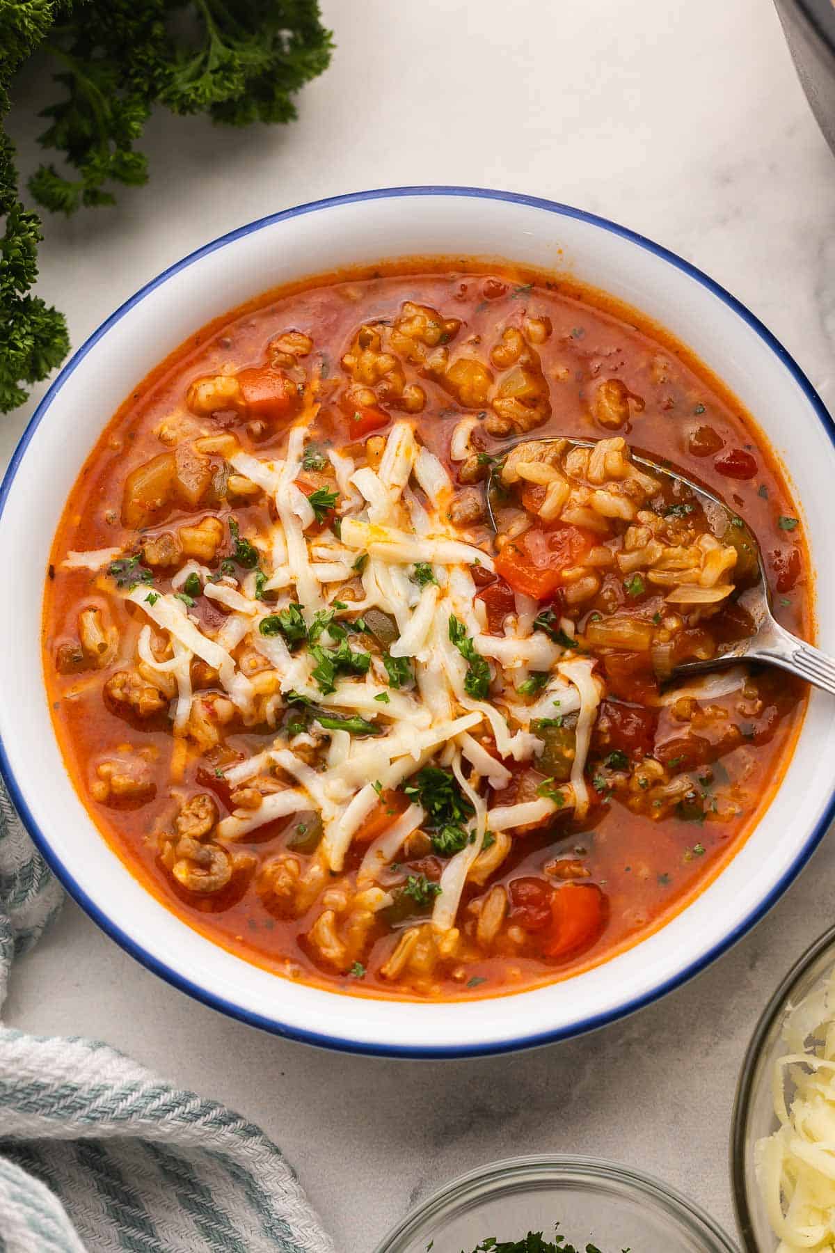 Stuffed Pepper Soup is a hearty, flavor-packed soup made with Italian sausage, bell peppers, long grain rice, and tomatoes. It’s an easy, healthy, one-pot dinner that you can make on the stove top or in a slow cooker! #soup #recipe #dinner | dinner ideas | soup recipes | easy recipes | healthy soup | healthy dinner | italian sausage | healthy dinner | soup recipe a white and blue bowl with stuffed pepper soup topped with shredded cheese.