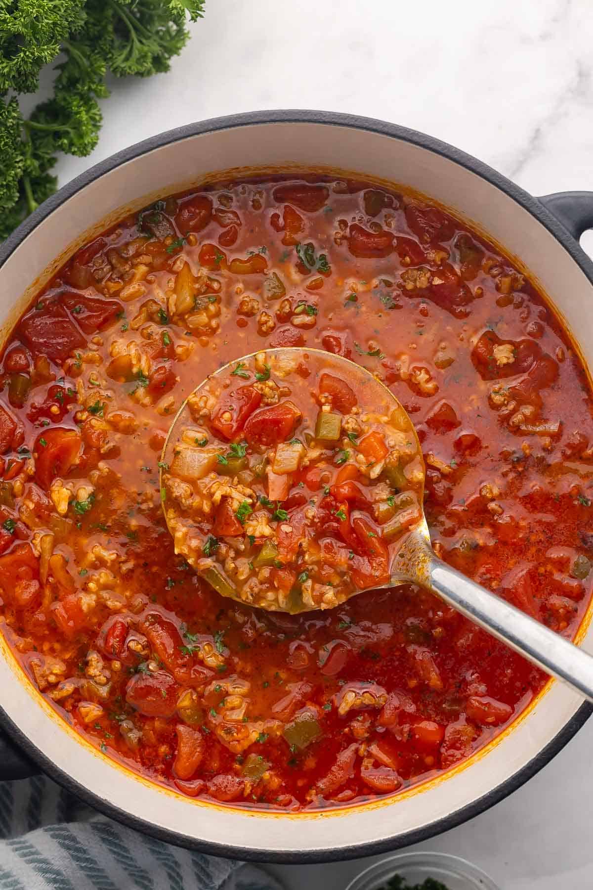 Stuffed Pepper Soup is a hearty, flavor-packed soup made with Italian sausage, bell peppers, long grain rice, and tomatoes. It’s an easy, healthy, one-pot dinner that you can make on the stove top or in a slow cooker! #soup #recipe #dinner | dinner ideas | soup recipes | easy recipes | healthy soup | healthy dinner | italian sausage | healthy dinner | soup recipe a steel ladle scooping stuffed pepper soup out of large pot.