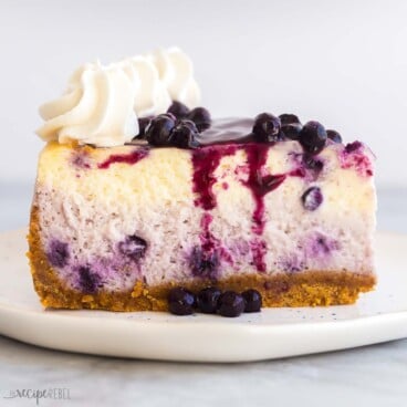 square image of a slice of blueberry cheesecake on a white plate.