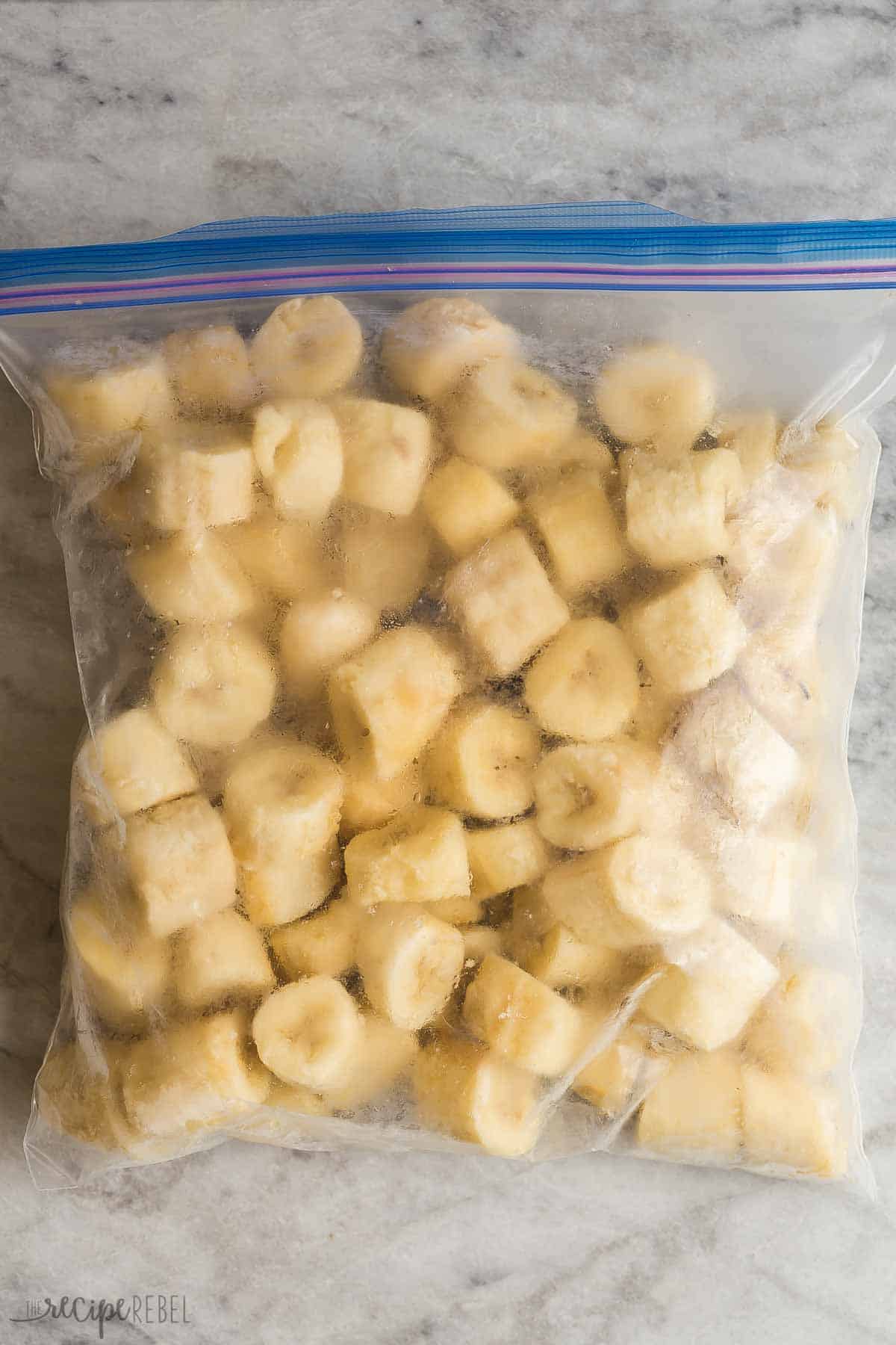 How to freeze bananas 3 different ways, which means you can stock up and have less waste. Perfect for baking, smoothies, cold drinks and more! #banana #bananas #mealprep #baking | food prep | how to freeze fruit | banana recipes | baking with bananas | freezing tips sliced frozen bananas in freezer bag on a marble background.
