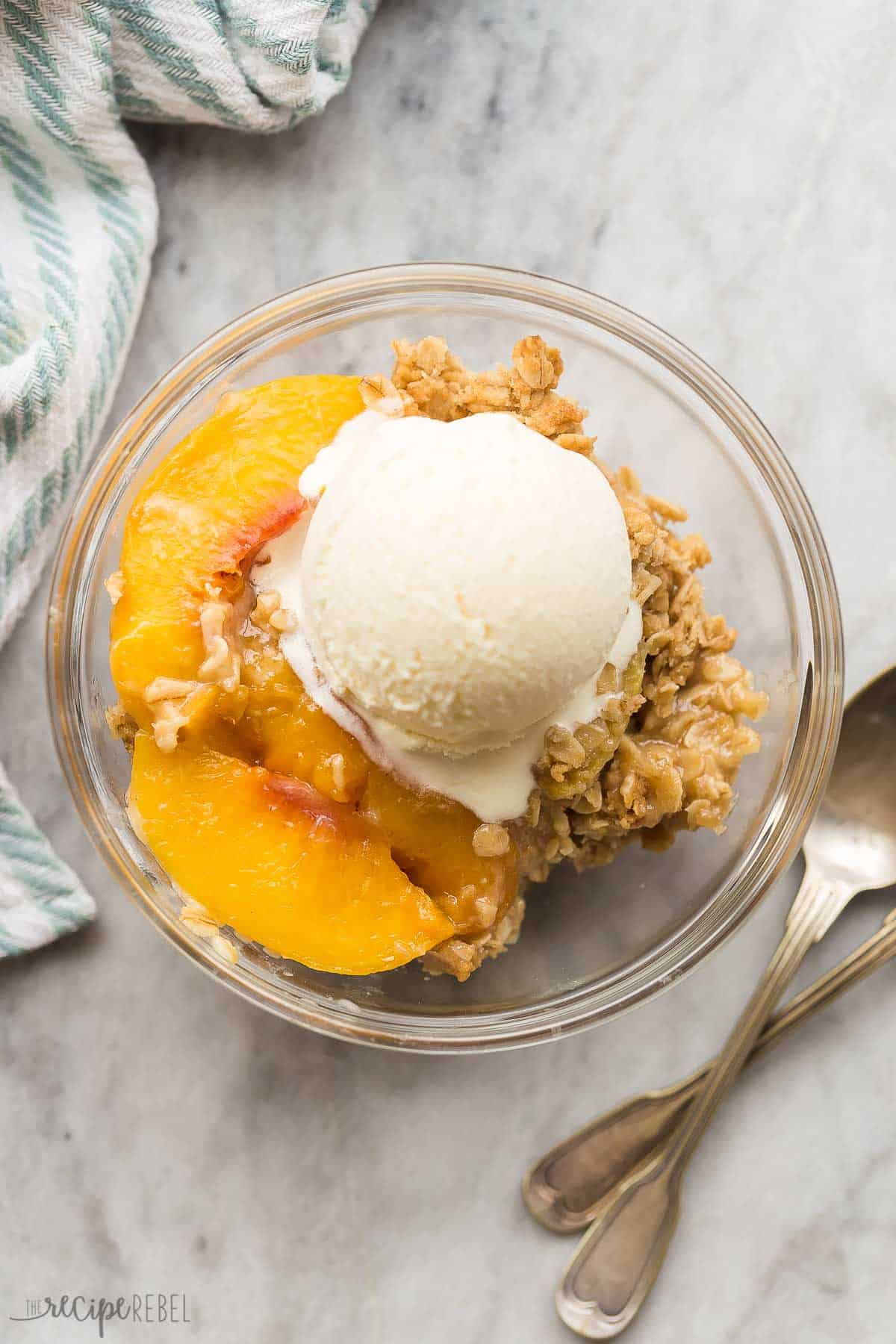 This easy Peach Crisp is made with fresh, canned or frozen peaches, plus a crunchy brown sugar oat topping! It's make ahead and freezer friendly -- the perfect peach dessert for summer. #peach #dessert #recipe | easy dessert recipes | fruit crisp | fruit desserts | warm dessert | peach dessert | peach recipes | summer recipes overhead image of peach crisp in a glass bowl with vanilla ice cream.