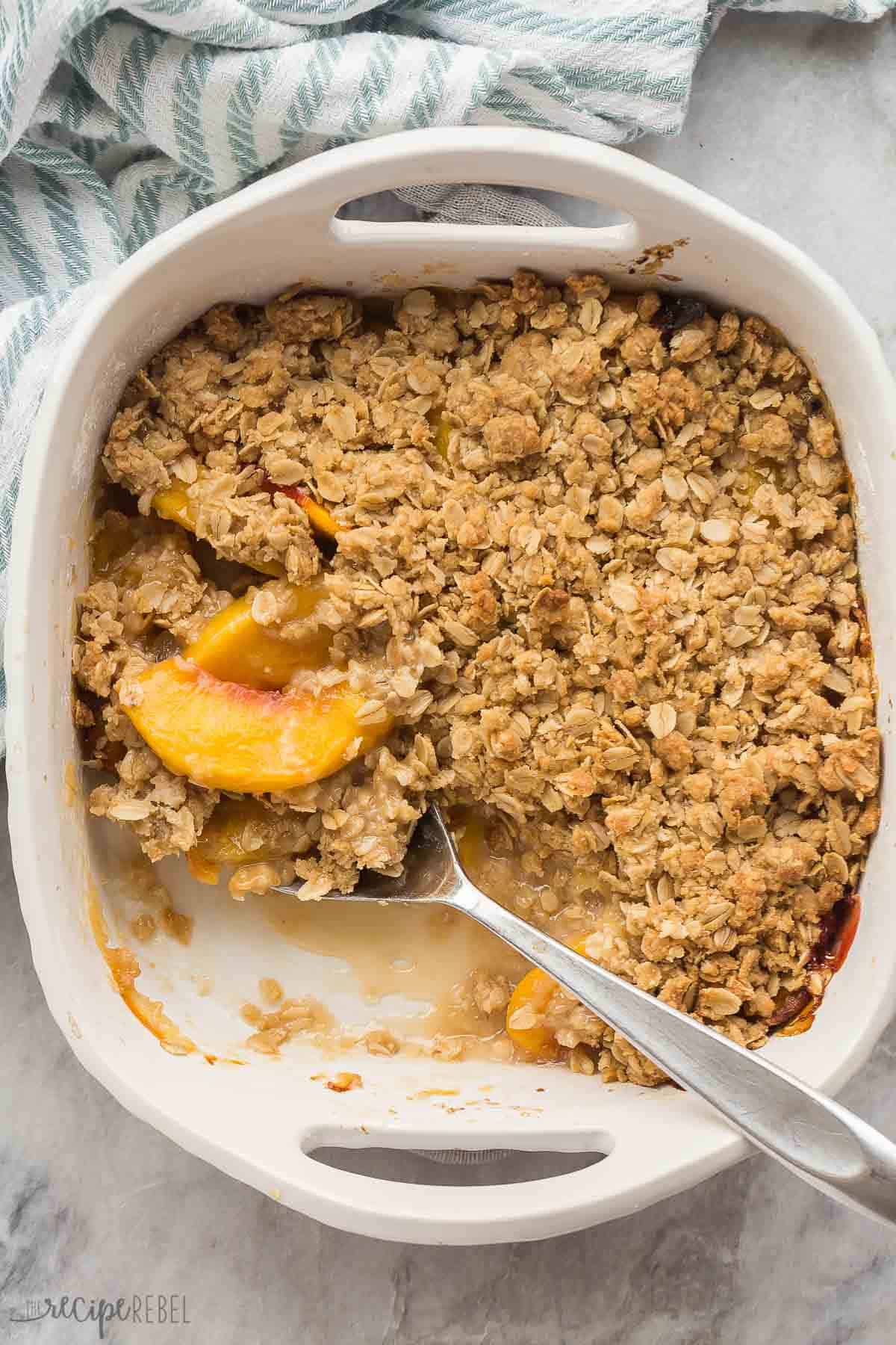 This easy Peach Crisp is made with fresh, canned or frozen peaches, plus a crunchy brown sugar oat topping! It's make ahead and freezer friendly -- the perfect peach dessert for summer. #peach #dessert #recipe | easy dessert recipes | fruit crisp | fruit desserts | warm dessert | peach dessert | peach recipes | summer recipes overhead image of a full pan of peach crisp with scoop missing.