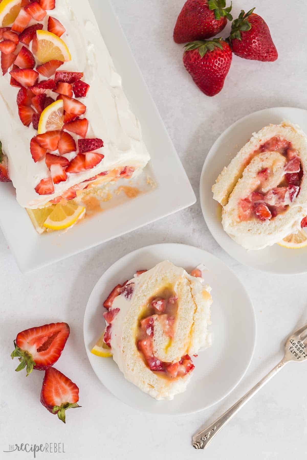 This Strawberry Lemon Angel Food Cake Roll is an easy dessert made with angel food cake mix, fresh lemon curd, and loads of fresh strawberries! The perfect easy summer dessert! #strawberry #lemon #cake #recipe #dessert | easy dessert recipes | angel food cake recipes | roll cake | summer dessert | lemon desserts | strawberry desserts | cake mix hacks overhead image of strawberry lemon angel food cake roll with two slices cut and on white plates.