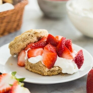 square image of strawberry shortcake dessert with biscuit, whipped cream and fresh strawberries on a white plate.