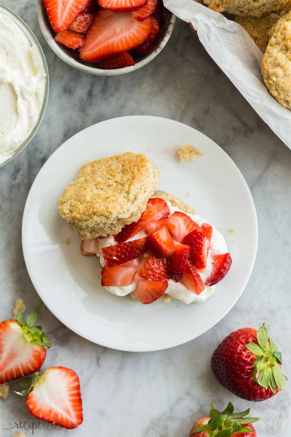 This Strawberry Shortcake recipe is made completely from scratch, but make ahead and freezer options make this an easy strawberry dessert you'll enjoy all summer long! With flaky biscuits, fresh strawberries and homemade whipped cream. #strawberry #dessert #recipe | dessert recipes | easy desserts | summer dessert | strawberry recipes | dessert recipes | baking from scratch | homemade whipped cream | make ahead overhead image of strawberry shortcake dessert on a white dessert plate.