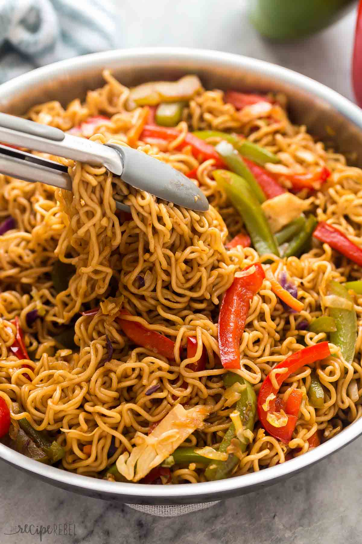 This Vegetable Lo Mein is made with 6 ingredients and packed with flavor and veggies! Easily customizable to your tastes and made it 20 minutes. #recipe #dinner #vegetarian | dinner ideas | dinner recipes | vegetarian recipes | meatless meals | ramen | asian food | takeout close up image of tongs scooping veggie lo mein from steel skillet.