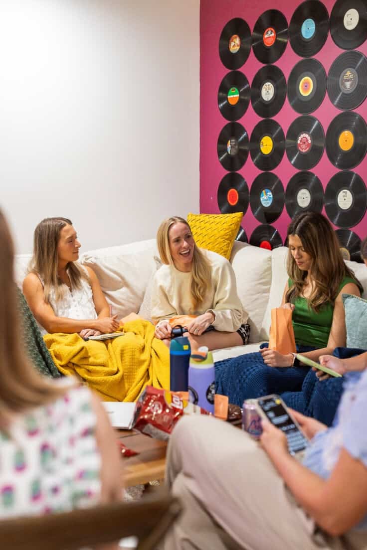 women talking in a living room with records on the wall.