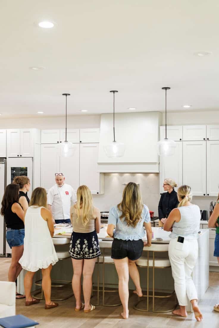 group of women standing in a kitchen listening to a chef.