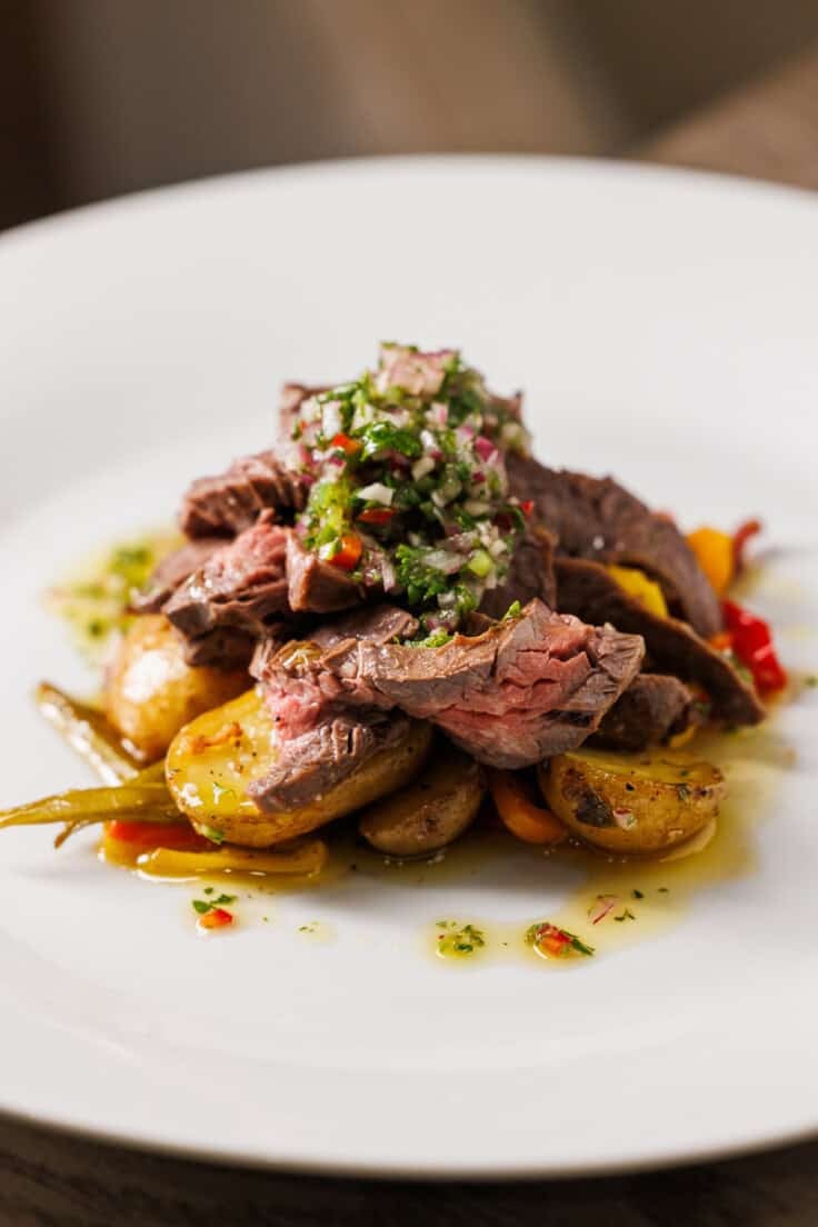 potatoes steak and chimichurri on a white plate.