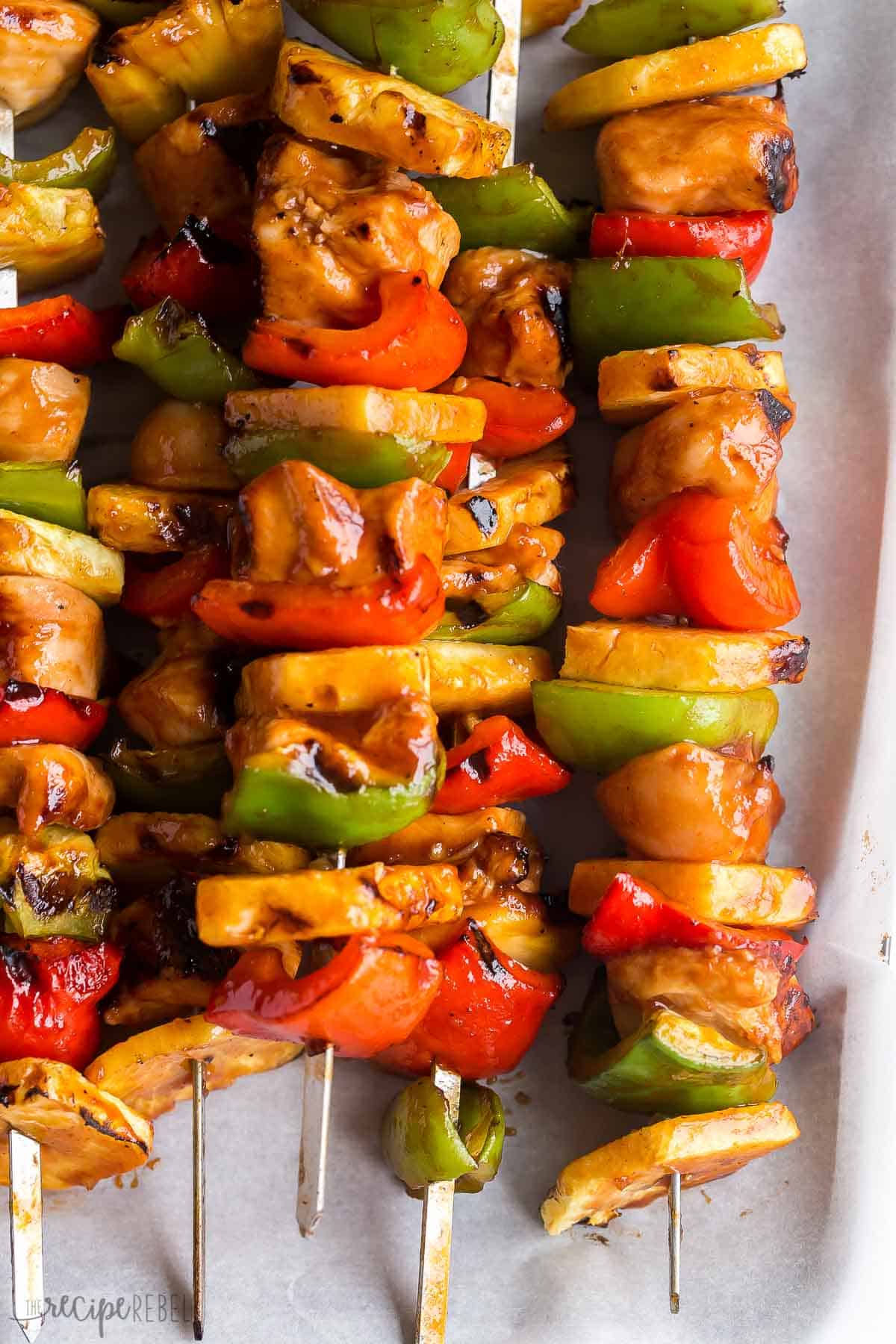 These Hawaiian Chicken Kabobs are sweet and savory, loaded with tender chicken breast, pineapple chunks, bell peppers and an easy pineapple BBQ marinade! The perfect prep-ahead summer meal. #chicken #chickenbreast #kabob #grilling #dinner | easy dinner ideas | dinner recipes | chicken recipes | grilled chicken | summer grilling | summer dinner close up image of chicken pineapple and pepper skewers on parchment.