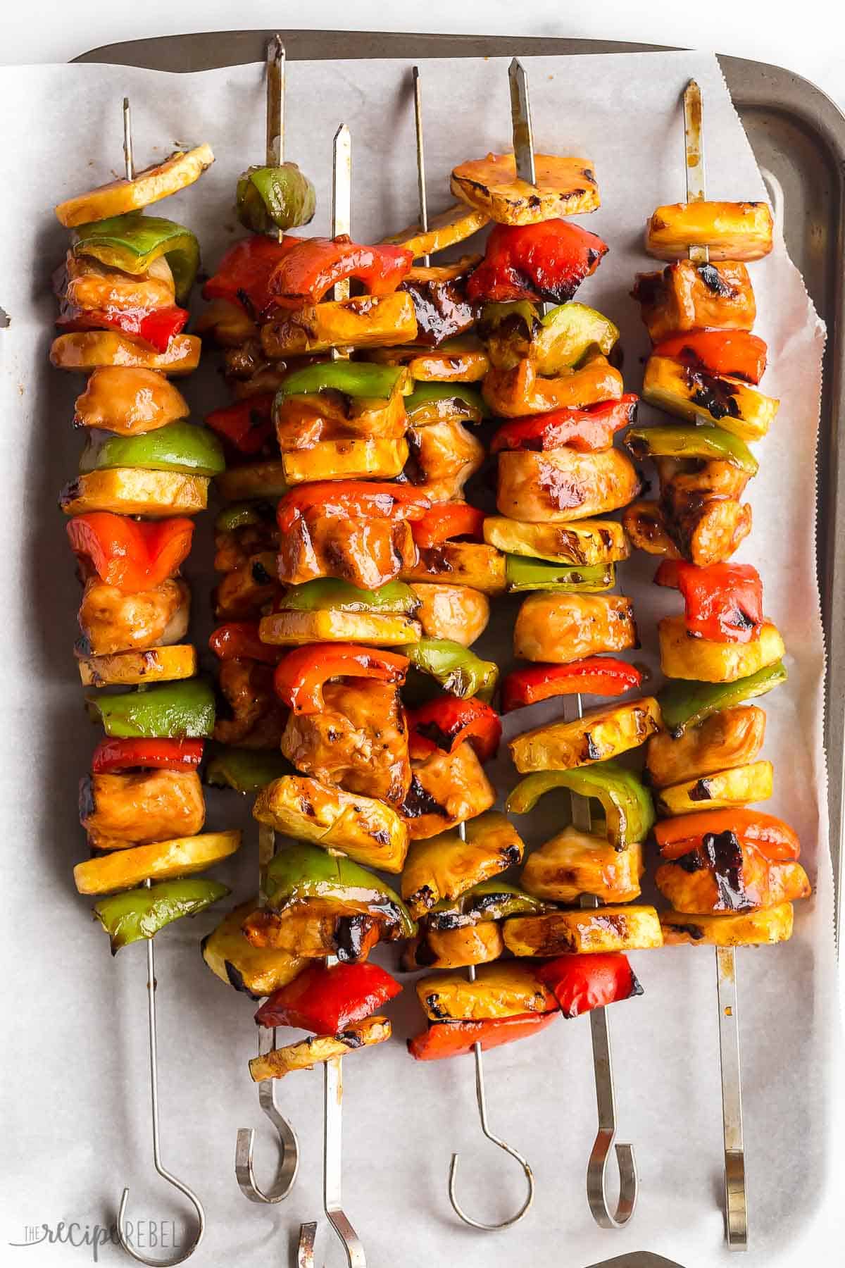 These Hawaiian Chicken Kabobs are sweet and savory, loaded with tender chicken breast, pineapple chunks, bell peppers and an easy pineapple BBQ marinade! The perfect prep-ahead summer meal. #chicken #chickenbreast #kabob #grilling #dinner | easy dinner ideas | dinner recipes | chicken recipes | grilled chicken | summer grilling | summer dinner cooked hawaiian chicken kabobs on parchment lined pan with pineapple and peppers.