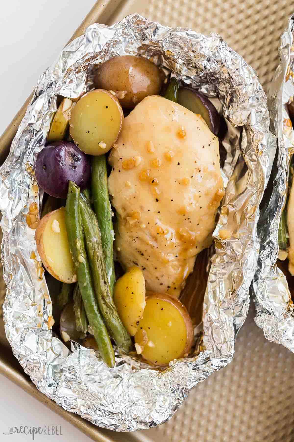 These Honey Garlic Chicken Foil Packets are made with juicy grilled chicken breast, potatoes and green beans and covered in the simplest homemade honey garlic sauce -- an easy camping meal perfect for summer dinners! close up image of one honey garlic chicken foil pack with potatoes and green beans.