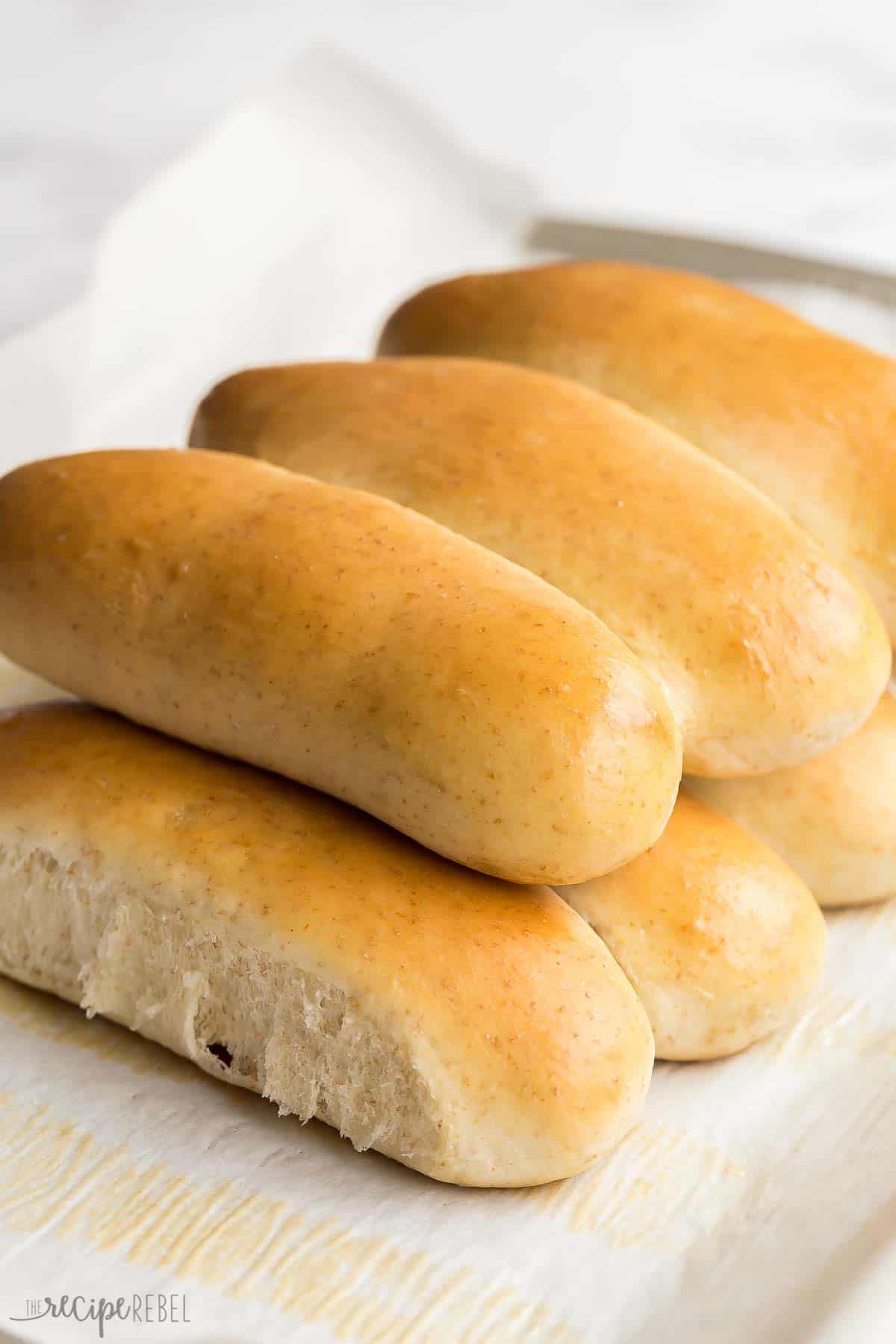 These Homemade Hot Dog Buns will take your barbecue to the next level! They are soft and fluffy and way better than store bought! #hotdog #barbecue #bread #baking #recipe | easy baking recipes | homemade hot dog buns | homemade buns | baking from scratch | barbecue recipes | easy recipes homemade hot dog buns stacked on a baking sheet.