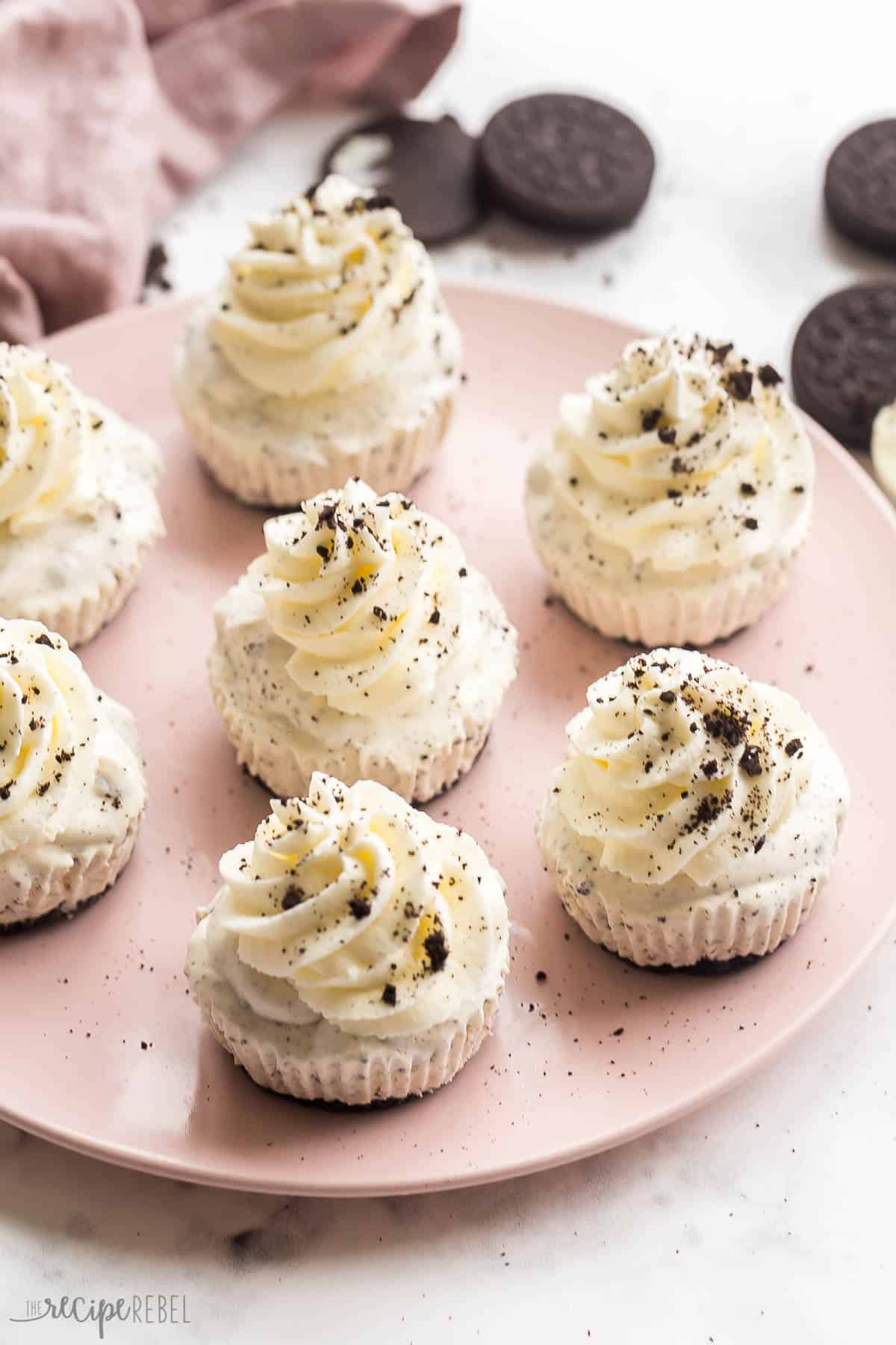 These No Churn Oreo Ice Cream Cupcakes are an easy, 4-ingredient, no bake summer treat perfect for a party! Switch up the cookie flavors for your favorites. #icecream #dessert #recipe | dessert recipes | ice cream recipes | no churn ice cream | oreo ice cream | oreo desserts | easy summer dessert | easy recipes pink plate with oreo ice cream cupcakes with whipped cream and crushed oreos.
