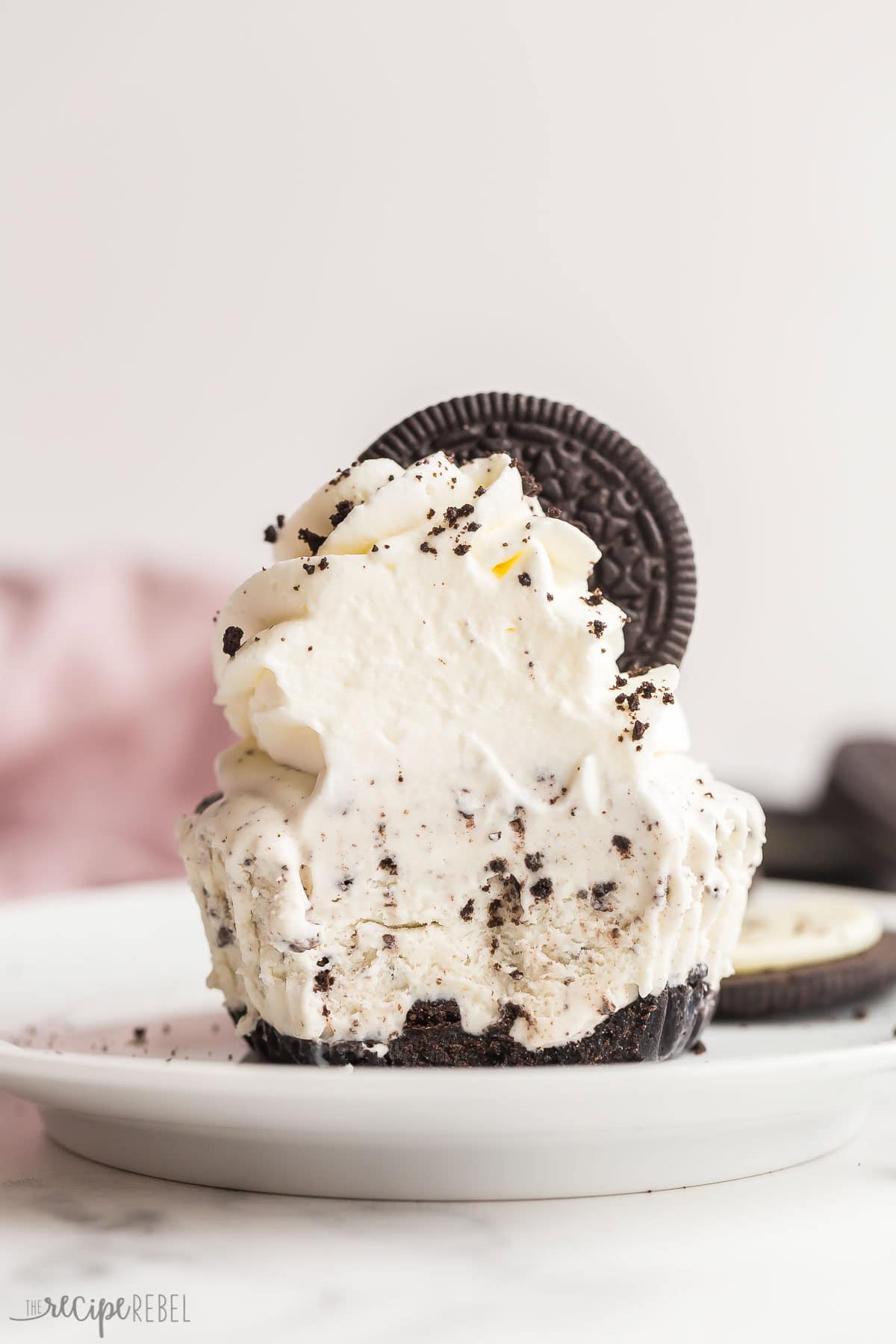 These No Churn Oreo Ice Cream Cupcakes are an easy, 4-ingredient, no bake summer treat perfect for a party! Switch up the cookie flavors for your favorites. #icecream #dessert #recipe | dessert recipes | ice cream recipes | no churn ice cream | oreo ice cream | oreo desserts | easy summer dessert | easy recipes small white plate with oreo ice cream cupcake on it with whipped cream on top.