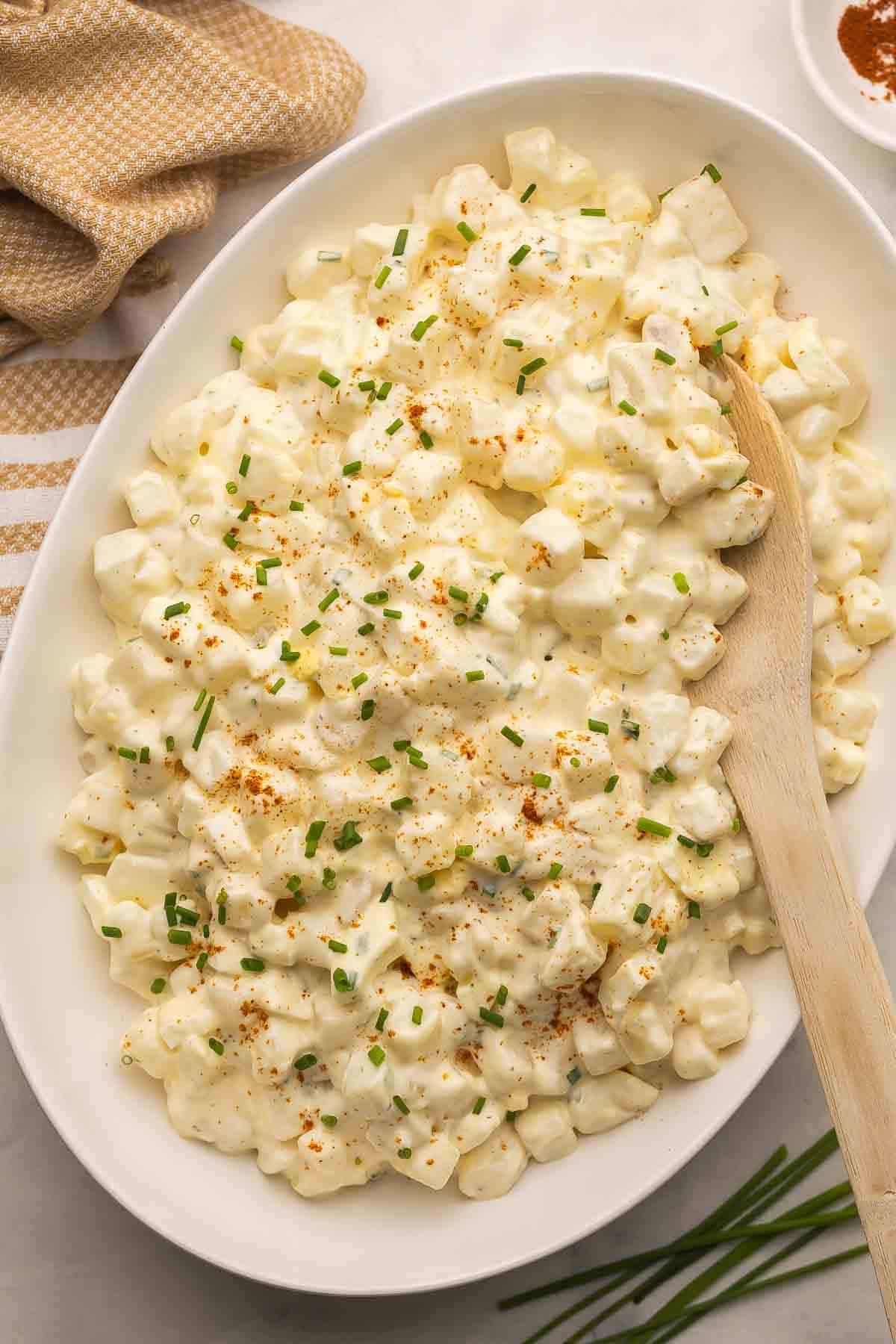 Easy Potato Salad is a classic recipe made with red potatoes, eggs, and a tangy, creamy dressing. It's a great side dish that's simple, easy to make ahead, and BBQ-ready! #salad #bbq #recipe #dinner | side dishes | summer side dish recipes | bbq sides | make ahead salad | salad recipes | potato recipes | easy recipes overhead image of large platter of potato salad with wooden spoon stuck in.